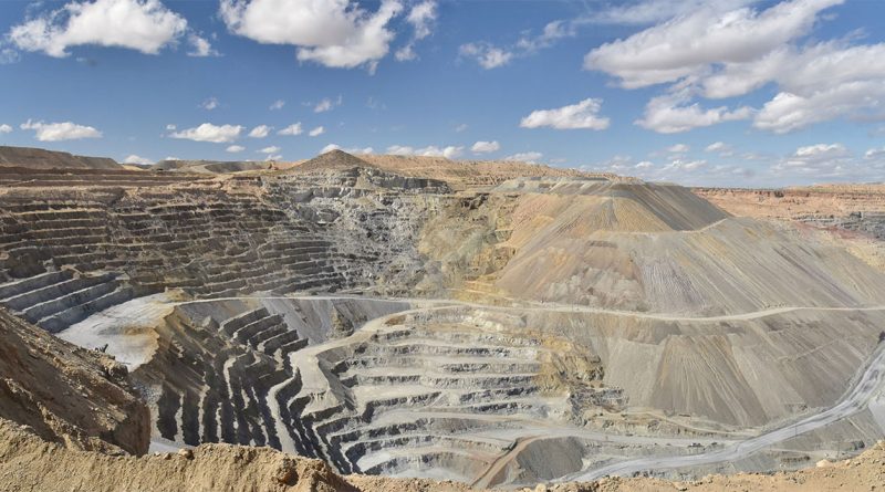 Open-pit copper mine under a blue sky with terraced rock layers, showcasing large-scale mineral extraction in a desert environment.