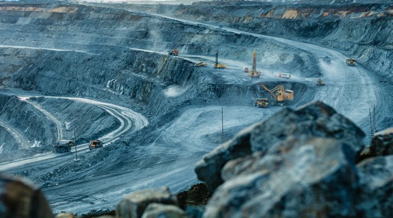Large open-pit mine with terraced rock walls and haul trucks operating on winding roads across the excavation site.